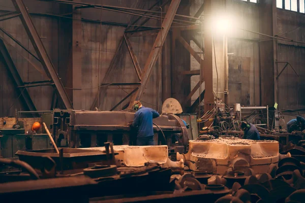 Werknemer in werkplaats verwerkt groot gietijzer na gieten in metallurgische gieterij — Stockfoto