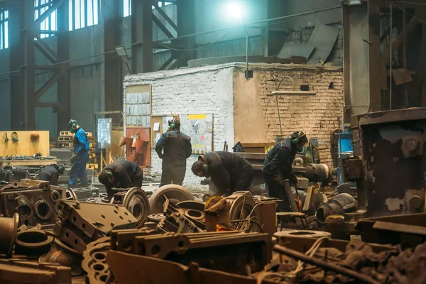 Arbetstagare i verkstad i metallverk bearbetar stora gjutjärnsdelar efter gjutning, tung industri — Stockfoto