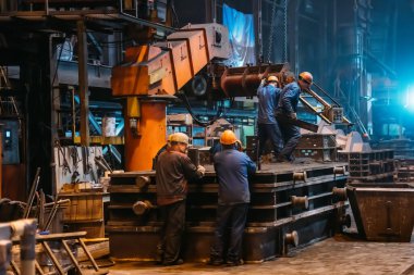 Çalışan işçiler çelik fabrikasına büyük küf demirleri döküyorlar.