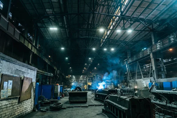 Soldador trabaja en taller industrial. Destellos blancos y humo de soldadura — Foto de Stock