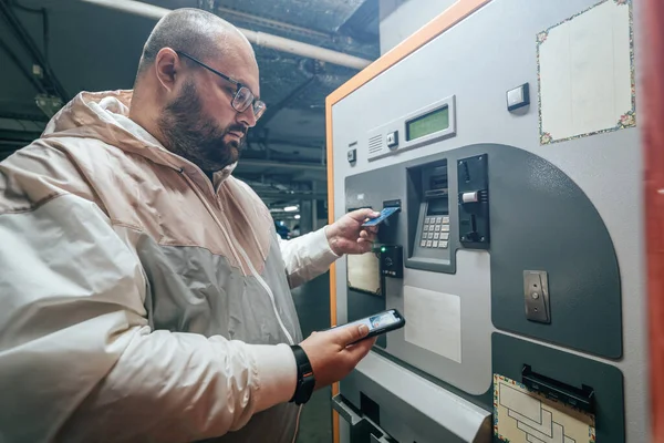 Hombre paga por estacionamiento subterráneo en el centro comercial terminal de pago automático utilizando su teléfono o tarjeta —  Fotos de Stock