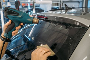 Profesyonel temizleyici, araba camına boya sürmek için endüstriyel kurutma makinesiyle renkli film ısıtıyor.