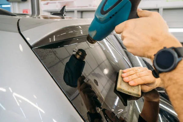 O detalhador profissional aquece o filme de matiz com secador industrial para aplicar a tintura no vidro do carro, close-up — Fotografia de Stock