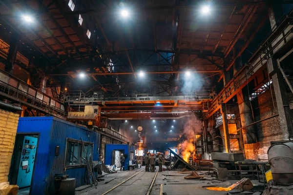 Steel production at metallurgical plant, large workshop with beam cranes and underground blast furnace