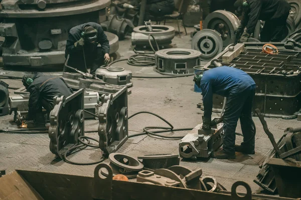 Große Werkstatt mit Hüttenarbeitern, die mit Gussteilen arbeiten, Nachgussbearbeitung in der Stahlgießerei — Stockfoto