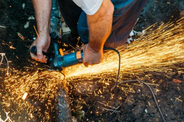 İşçi öğütücüyle gaz borusunu kesiyor ve bir sürü kıvılcım uçuşuyor.