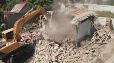 Hidrolik kazı kovası harap olmuş evi yok ediyor. Binanın yıkılması, hava manzarası.