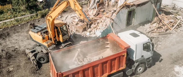 Ekskavator memuat puing-puing konstruksi bangunan tua setelah kehancuran dalam truk sampah, pandangan udara — Stok Foto