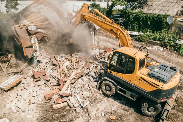 Penghancuran bangunan oleh ekskavator industri. Bucket istirahat dinding dan atap rumah tua penuh debu, pandangan udara — Stok Foto