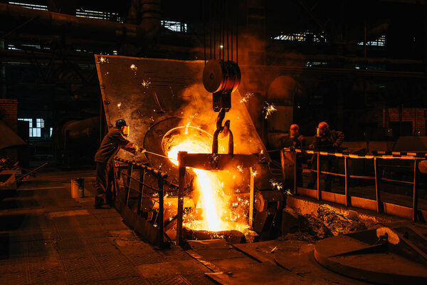 Iron casting. Molten metal pouring from blast furnace into ladle. Steel production in foundry workshop. Metallurgical plant, heavy industry