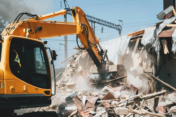 Destruction of old house by excavator. Bucket of excavator breaks concrete structure