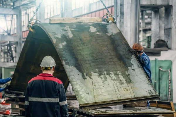 Trabajadores irreconocibles en planta metalúrgica descargan chapas de acero o metal con grúa — Foto de Stock