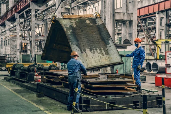Pekerja tak dikenal di pabrik metalurgi membongkar baja atau lembaran logam dengan derek — Stok Foto