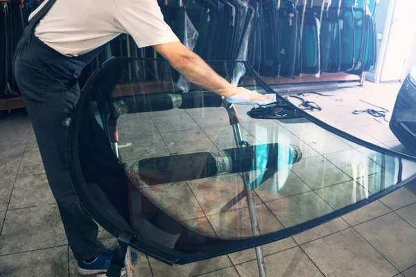 Automobile glazier worker degreases glass windscreen or windshield before installation on car in service station garage — Fotografia de Stock