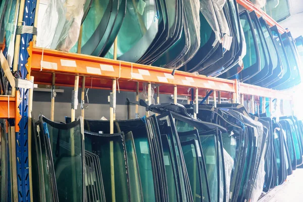 Lots of windshields for different cars on service station shelves ready to install or replace broken glass with cars — Stock Fotó