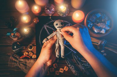 Büyücü ya da cadı pentagram, yanan mumlar ve diğer okült nesnelerin bulunduğu ritüel masasındaki vudu bebeğine iğne batırıyor. Vudu büyücülüğü, maneviyat ve okültizm kavramı
