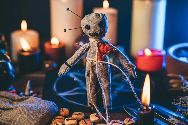Boneka Voodoo diisi dengan jarum di meja ajaib dengan lilin dan benda gaib. Sihir dan ritual seram gelap. Balas dendam melalui konsep sihir. Stok Gambar Bebas Royalti