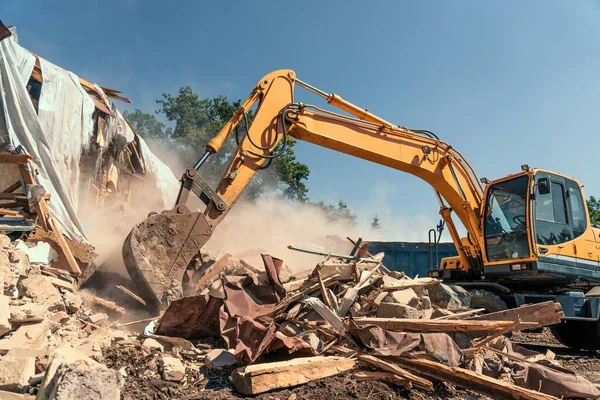 Penghancuran rumah tua oleh penggali dengan banyak debu. Ember ekskavator menghancurkan struktur beton Stok Gambar