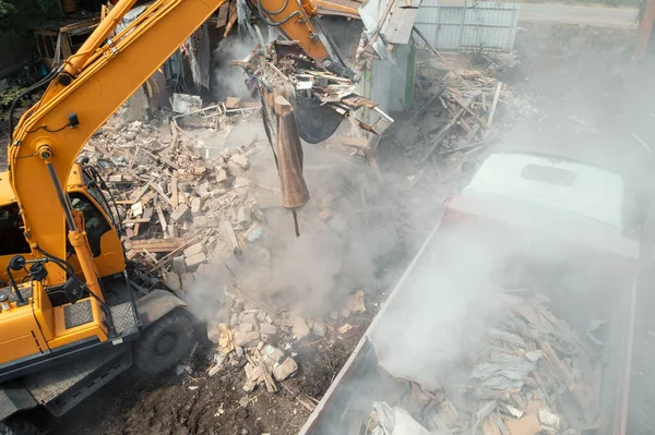 Excavator bucket loads industrial debris into truck. Process of demolishing and destruction old house. Release of quarters for new development