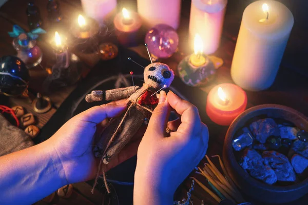 Penyihir atau penyihir menusukkan jarum ke dalam boneka voodoo di meja ritual dengan pentagram, membakar lilin dan benda okultisme lainnya, pemandangan atas. Ilmu sihir voodoo, spiritualitas dan konsep okultisme Stok Gambar
