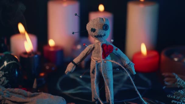 Voodoo Magic concept. Voodoo doll studded with needles with pierced rag heart and around burning candles. Spooky or eerie magical esoteric ritual — Stock Video