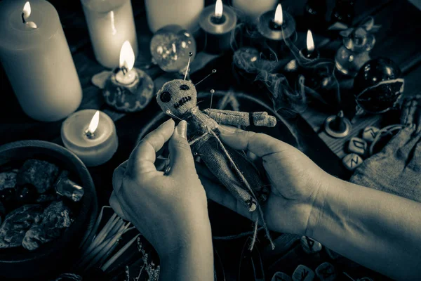 Sorceress or witch sticks needles into voodoo doll at ritual table with pentagram, burning candles and other occult objects. Voodoo witchcraft, spirituality and occultism concept — Stock Photo, Image