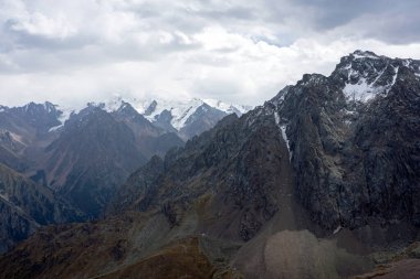 Zailiysky Alatau sıradağlarındaki karlı dağ zirveleri ve kayalık tepelerin panoramik görüntüsü