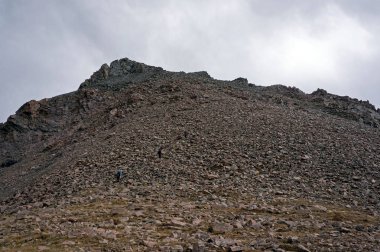 Maceracı yürüyüşçüler Shymbulak 'ın yukarısındaki yüksek dağlık arazide dik kayalık bir dağa tırmanıyorlar.