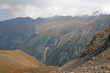 Zailiyskiy Alatau 'nun uçsuz bucaksız dağ manzarası. Yuvarlanan tepeler ve bulutlu gökyüzünün altında karla kaplı tepeler.
