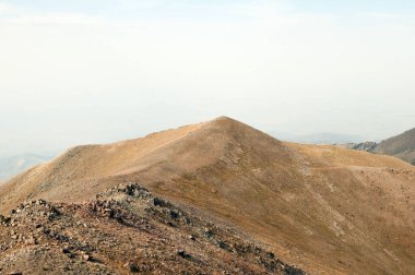 Puslu gökyüzünün altındaki Tian Shan dağlarının sarp kayalık yamaçlarından geçen dar patikalar.