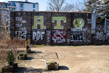Renkli grafiti ve etiketlerle kaplı kırmızı tuğlalı bir duvarın ön görüntüsü. Önemli unsurlar arasında büyük yeşil 
