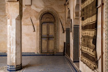 Fes Medina, Fas 'taki Palais El Glaoui' nin (Dar Glaoui) iç kesiminin çarpıcı bir görüntüsü. Görüntü, iki antik mukhala tüfeği tarafından çevrelenmiş muhteşem bir alçı kemeri tarafından çerçevelenmiş, karmaşık şekilde oyulmuş ahşap bir kapı yakalıyor. Zemin ve duvarlar da öyle.