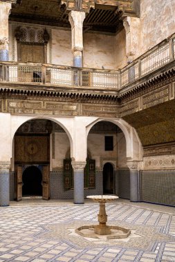 Fes Medina 'daki Palais El Glaoui' nin iç avlusunun çarpıcı manzarası. Fotoğraf, geometrik zellij döşeme, merkezi bir mermer çeşme ve karmaşık mozaikler ve oyulmuş sıva ile süslenmiş duvarları vurguluyor. Zarif kemerler ve fayanslarla kaplı