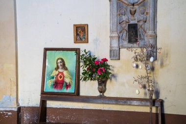 Kırsal bir İtalyan evindeki küçük bir sunağın samimi bir görüntüsü. Resimde, İsa 'nın Kutsal Kalbi' nin ahşap bir rafta duran çerçeveli bir resmi, bir vazo taze çiçeğin yanında ve süslenmiş geleneksel bir 