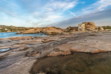 Punta Tegge 'nin La Maddalena adasındaki panoramik manzarası. Görüntü, Maddalena Takımadaları Ulusal Parkı 'nın karakteristik bir özelliği olan rüzgar heykeli şeklindeki engebeli bir kıyı manzarasına karşı kurulmuş antik bir taş gözlem kulesini gösteriyor..