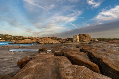 Punta Tegge 'nin La Maddalena adasındaki panoramik manzarası. Görüntü, Maddalena Takımadaları Ulusal Parkı 'nın karakteristik bir özelliği olan rüzgar heykeli şeklindeki engebeli bir kıyı manzarasına karşı kurulmuş antik bir taş gözlem kulesini gösteriyor..