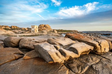 Punta Tegge 'nin La Maddalena adasındaki panoramik manzarası. Görüntü, Maddalena Takımadaları Ulusal Parkı 'nın karakteristik bir özelliği olan rüzgar heykeli şeklindeki engebeli bir kıyı manzarasına karşı kurulmuş antik bir taş gözlem kulesini gösteriyor..