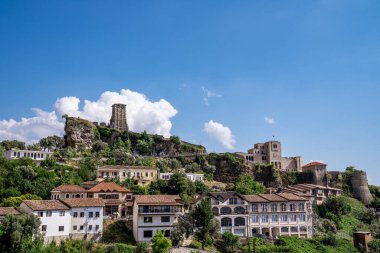 Ortaçağ Kruja Kalesi 'nin panoramik görüntüsü eski kasabanın üzerinde yükseliyor. Görüntü, kalenin duvarları içine inşa edilen Ulusal Skanderbeg Müzesi 'ni, antik saat kulesini ve açık mavi gökyüzünün altında bulunan geleneksel taş evleri sergiliyor.