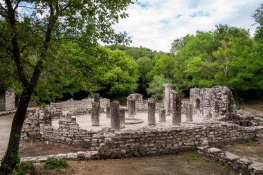 M.S. 6. yüzyılın başlarında, UNESCO 'nun Dünya Mirası' na ait Butrint arkeoloji sahasında yer alan erken dönem Hıristiyan Baptisterisi 'nin sütunları ve dairesel duvarlarına zemin seviyesinde bir bakış. Yapı, yemyeşil Akdeniz ormanlarının içine kuruludur.