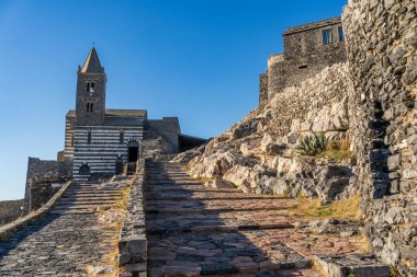 İkonik çizgili Gotik-Romen mimarisi ve Porto Venere 'deki Doria Kalesi' nin taş duvarlarıyla tarihi St. Peter Kilisesi 'nin büyüleyici güneşli manzarası. Bu UNESCO Dünya Mirası alanı Li Nehri üzerinde açık mavi bir gökyüzüne karşı ele geçirildi.