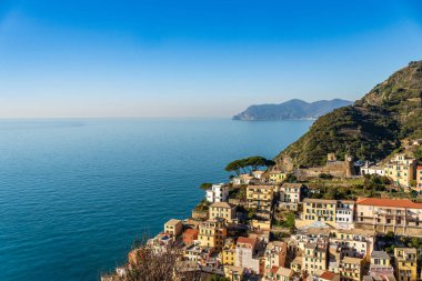 Teraslı tepeler ve kristal berrak Ligurya Denizi arasına kurulmuş Riomaggiore köyünün nefes kesici yüksek açılı görüntüsü. Fotoğraf, kasabanın renkli mimarisini ve Cinque Terre Ulusal Parkı sahil şeridinin vahşi güzelliğini yansıtıyor.,