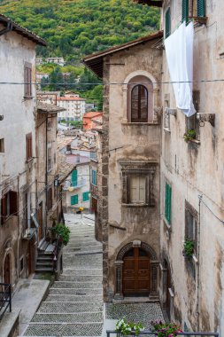 İtalya 'nın Scanno kentinin tarihi merkezinin otantik ve manzaralı bir manzarası. Fotoğraf, güneşte kuruyan beyaz çamaşırların, geleneksel basamaklı sokakların ve Abruzzo Nati 'nin yemyeşil dağlarının yer aldığı antik taş binalar arasında günlük yaşamı yakalıyor.