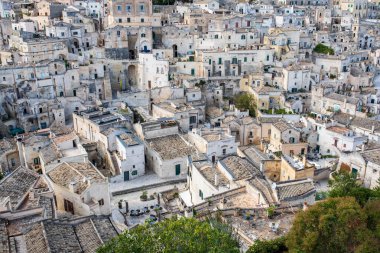 Matera 'nın kireçtaşı kayasına oyulmuş ve inşa edilmiş yoğun ev ağını gözler önüne seren muhteşem bir yüksek açılı çekim. Görüntü, bu antik troglodu karakterize eden bininci katman çatı, ara sokaklar ve küçük kareler (vicinati) vurgular
