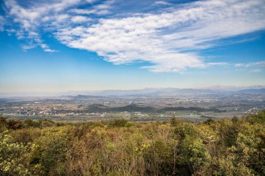 San Michele Dağı 'nın zirvesinden geniş panoramik manzara, Gorizia ili, Friuli Venezia Giulia. Görüntü, Julian Alpleri 'nin görkemli zirveleri tarafından arka planda çerçevelenmiş küçük köyler ve üzüm bağlarıyla kaplı Isonzo ovasını yakalıyor.