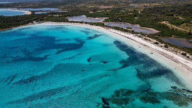 Sardinya, San Teodoro 'daki Lu Impostu plajını gösteren çarpıcı bir yüksek açılı drone görüntüsü. Fotoğrafta canlı turkuaz Akdeniz suları, el değmemiş beyaz kumlu kıyılar ve vahşi yeşil vejetaryenlerle çevrili eşsiz kıyı gölleri sergileniyor.