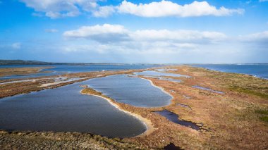 Sardunya 'daki Mistras Lagoon' un saf güzelliğini gösteren çarpıcı, yüksek açılı bir görüntü. Görüntü, sakin göl sularını Oristano Körfezi 'nden ayıran ve doğal kanalları ve tipik Akdeniz' i gösteren dar kum tükürüğünü gösteriyor.