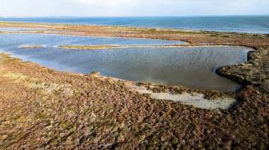 Sardunya 'daki Mistras Lagoon' un saf güzelliğini gösteren çarpıcı, yüksek açılı bir görüntü. Görüntü, sakin göl sularını Oristano Körfezi 'nden ayıran ve doğal kanalları ve tipik Akdeniz' i gösteren dar kum tükürüğünü gösteriyor.