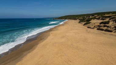 Avrupa 'nın en yüksek kum tepeleri arasında yer alan Arbus' taki Piscinas plajının panoramik hava manzarası. Görüntü, turkuaz deniz, uçsuz bucaksız altın kıyı şeridi ve yoğun bitki örtüsü arasındaki zıtlığı gösteriyor.