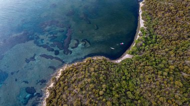 Caprera Adası 'ndaki Cala Bernardo plajının çarpıcı zenital panoramik drone görüntüsü. Fotoğraf turkuaz suların inanılmaz şeffaflığını, korunaklı bir körfeze demirlemiş tekneleri ve Maddalena Ar 'ın yemyeşil, el değmemiş Akdeniz çalılığını vurguluyor.