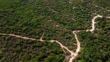 Baş döndürücü yukarıdan aşağıya doğru çekilmiş bir fotoğraf yoğun kıyı bitkilerinin derinliklerinde dolambaçlı toprak yollarda tek başına dolaşan beyaz bir karavan gösteriyor. Görüntü özgürlük, macera ve izolasyon temalarını somutlaştırarak sürdürülebilir t 'nin cazibesini vurguluyor